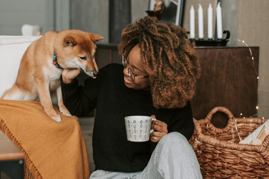 a woman sat on the floor holding a mug whilst patting her dog sat beside her.