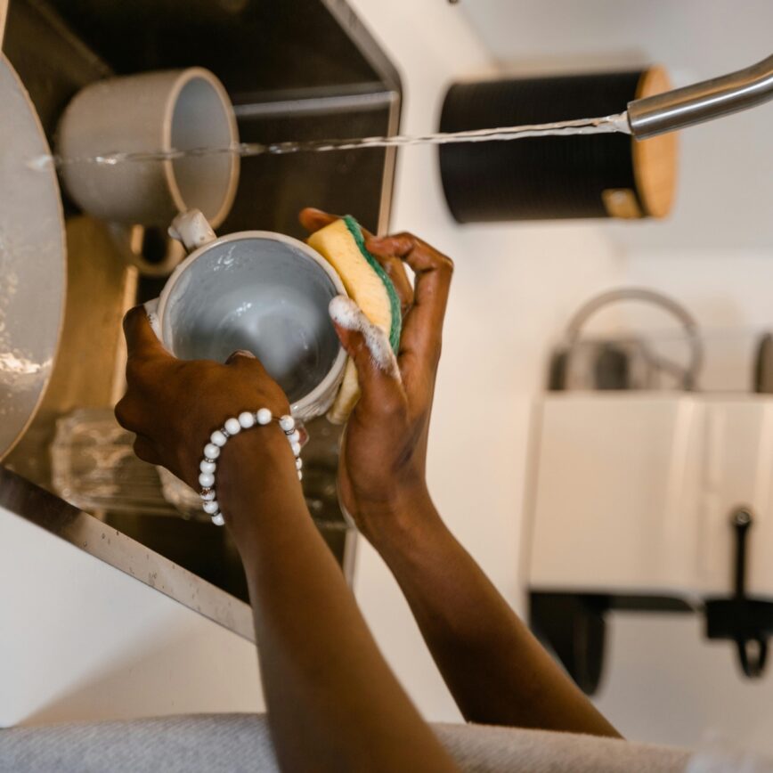 woman washing a mug over a silver sink using a sponge.