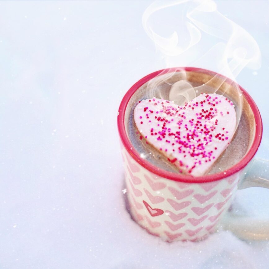 a mug with pink and red hearts with a warm drink and floating heart marshmallow.