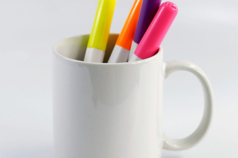 a white ceramic mug with various coloured pens being stored within it.