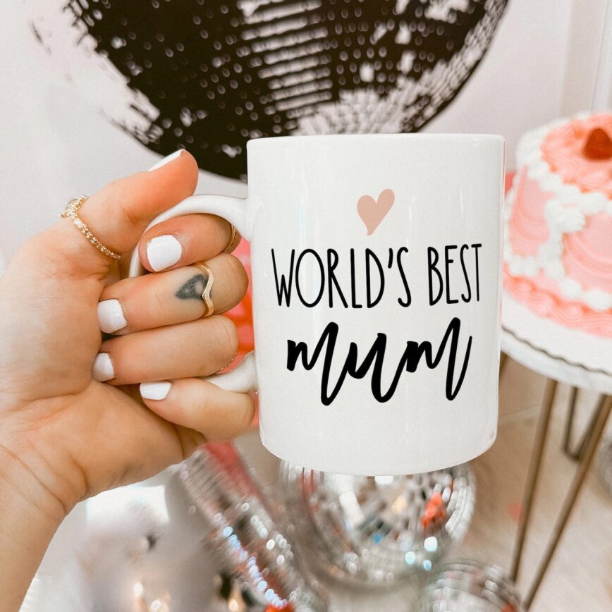 a white ceramic mug showing the text 'worlds best mum' below a pink heart illustration.